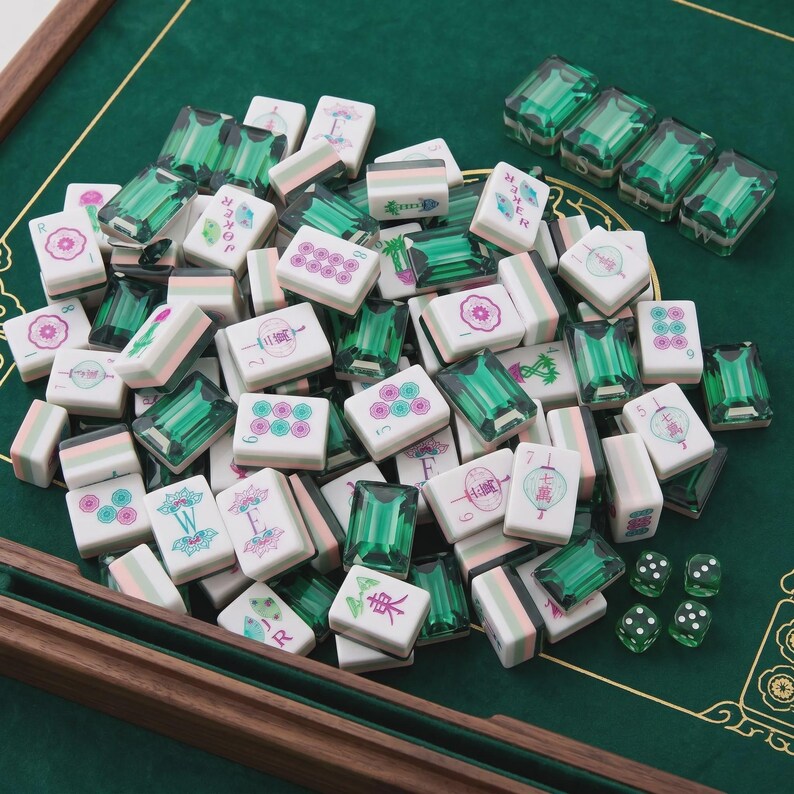 May include: A set of mahjong tiles featuring white faces with pink, green, and blue floral or character designs, paired with translucent emerald green backs. The collection includes several small green dice and four directional tiles.