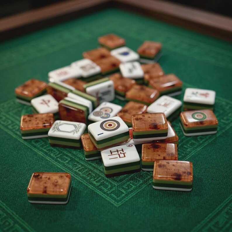 Pode incluir: Uma cole&ccedil;&atilde;o de pe&ccedil;as de mahjong com uma mistura de faces brancas com s&iacute;mbolos pretos e vermelhos e lados em camadas castanhos, verdes e brancos. As pe&ccedil;as est&atilde;o espalhadas numa pilha, exibindo v&aacute;rios caracteres, c&iacute;rculos e padr&otilde;es.