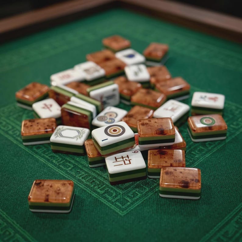 May include: A collection of mahjong tiles featuring a mix of white faces with black and red symbols and brown, green, and white layered sides. The tiles are scattered in a pile, displaying various characters, circles, and patterns on their top surfaces.