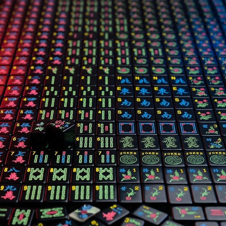 May include: A collection of black Mahjong tiles arranged in a grid, featuring vibrant neon-colored engravings of Chinese characters, numbers, directional symbols, and floral patterns, with some tiles scattered at the bottom of the frame.