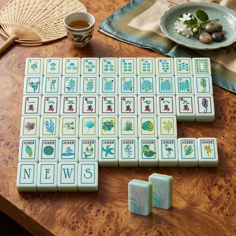 May include: A full Mahjong set with white tiles displaying diverse symbols and Chinese characters. The tiles are arranged on a wooden surface, with a cup of tea, a fan, and decorative elements in the background. The word "NEWS" is spelled out with tiles.
