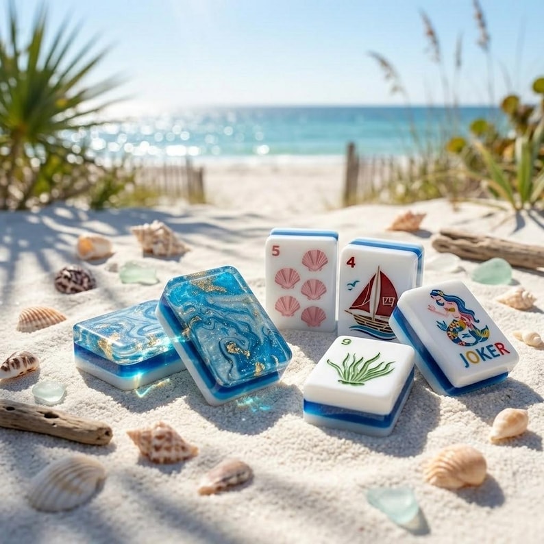 May include: A set of rectangular mahjong tiles featuring white bases with colorful illustrations of a sailboat, a mermaid labeled JOKER, pink seashells, and green seaweed, alongside two tiles with a blue and gold marbled resin top surface.