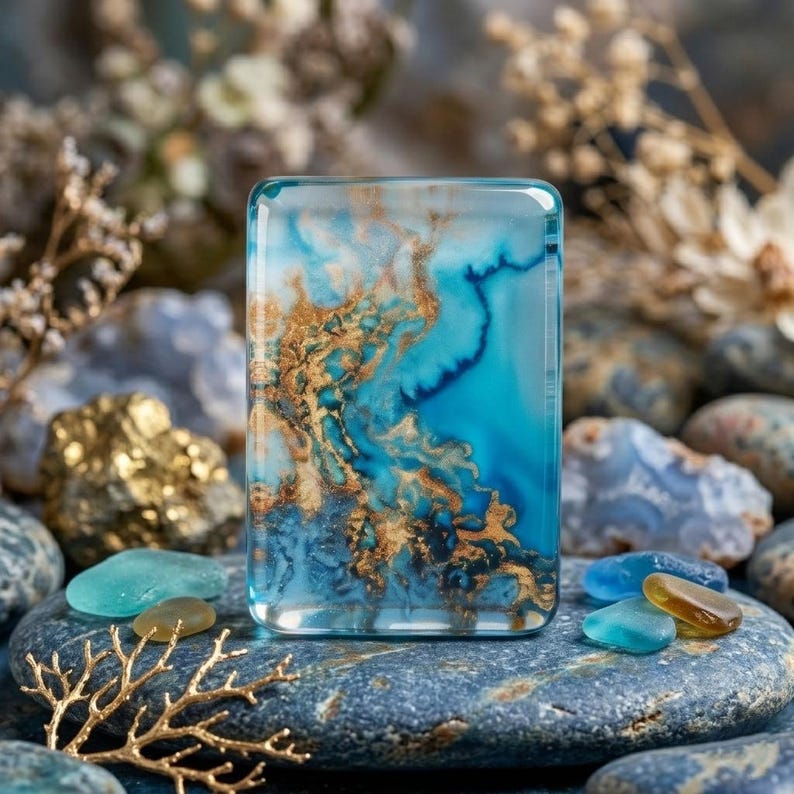 May include: A rectangular resin piece featuring a swirling pattern of deep blue, turquoise, and metallic gold veins. The surface is smooth and glossy, with a clear, glass-like finish that highlights the intricate, fluid color transitions throughout.