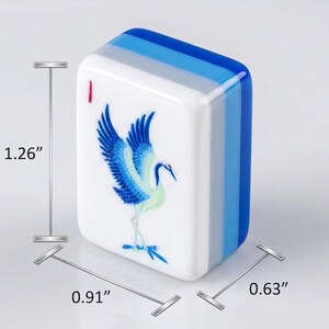 Op de afbeelding: Een rechthoekige mahjongtegel met een blauwe kraanvogelillustratie op een witte voorzijde en een effen blauwe achterzijde. De tegel is 3,2 cm hoog, 2,31 cm breed en 1,6 cm diep, met een kleine rode markering in de linkerbovenhoek.