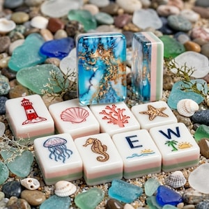 May include: A set of rectangular mahjong tiles featuring ocean-themed illustrations including a lighthouse, seashell, coral, starfish, jellyfish, seahorse, the letter E, and a palm tree with sun, alongside a tile with a blue and gold marbled pattern.