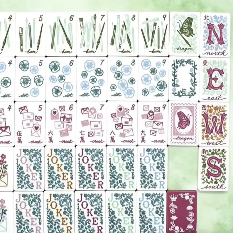 K&ouml;nnte beinhalten: Eine Sammlung von Mahjong-Steinen mit wei&szlig;en Vorderseiten und verschiedenen Illustrationen, darunter Kunstbedarf, Blumen, Umschl&auml;ge, Schmetterlinge und Richtungsbuchstaben. Die Steine zeigen Zahlen, chinesische Schriftzeichen und das Wort Joker in Blumenmustern.