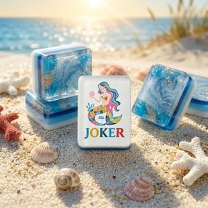 May include: A rectangular white tile featuring a colorful illustration of a mermaid holding a pink pearl above the word JOKER in multicolored letters, surrounded by several translucent blue and white resin blocks with gold flakes.