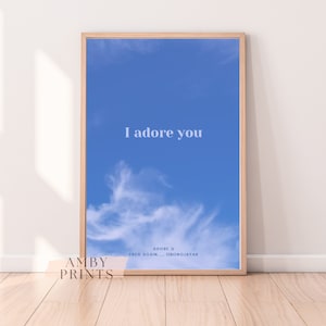 Könnte beinhalten: Ein gerahmter Druck mit blauem Himmel und weißen Wolken. Der Text "I adore you" ist in Weiß auf dem Druck geschrieben. Der Text "ADORE U FRED AGAIN... OBONGJAYAR" ist in Weiß am unteren Rand des Drucks geschrieben.