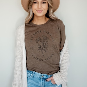 May include: A brown t-shirt with a floral design and the text "Set your mind on things above".