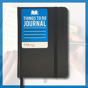 Puede incluir: Un diario negro "Things To Do" con una etiqueta azul y blanca. La etiqueta dice "Things To Do Journal" e incluye el texto "Organice sus citas, Enumere objetivos a corto y largo plazo, Planifique su día de manera efectiva, 144 páginas."