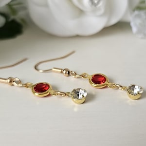 May include: Gold dangle earrings with a red and clear crystal design.