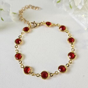 May include: A gold chain bracelet with red gemstone accents. The bracelet has a lobster clasp closure.