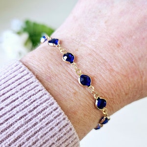 May include: A gold chain bracelet with dark blue faceted gemstone accents.