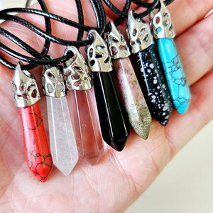 May include: Seven crystal point pendants on black cords. The pendants are in various colours, including red, white, pink, black, brown, and blue. Each pendant has a silver filigree design.