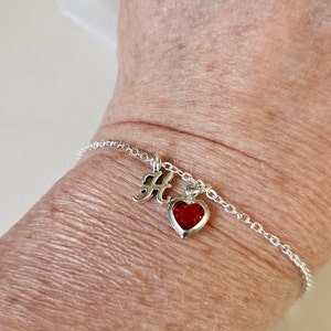 May include: A silver chain bracelet with a red heart charm and a silver charm with the letter "H" on it.