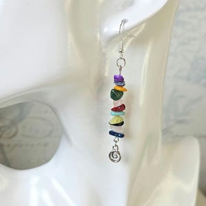 May include: A pair of silver dangle earrings with a spiral charm at the bottom. The earrings feature a variety of colourful gemstone beads, including purple, yellow, green, red, blue, and white.