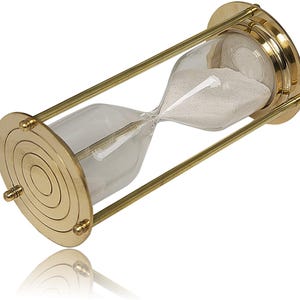 May include: An hourglass featuring a clear glass bulb filled with white sand, encased in a polished brass frame. The frame consists of two circular brass end caps with concentric ring engravings, connected by three slender brass support rods.