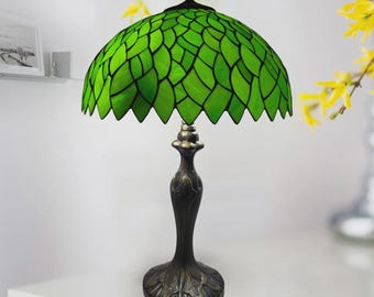 May include: A green stained glass table lamp with a leaf design. The lamp has a dark bronze base and stem. The shade is a vibrant green color, with a scalloped edge. The lamp is a decorative lighting fixture.