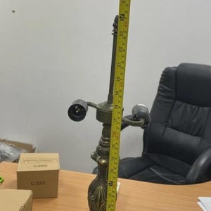 May include: An antique brass table lamp, approximately 29 inches tall, with a detailed floral base and two light sockets. The lamp is on a wooden desk, with a measuring tape alongside it.