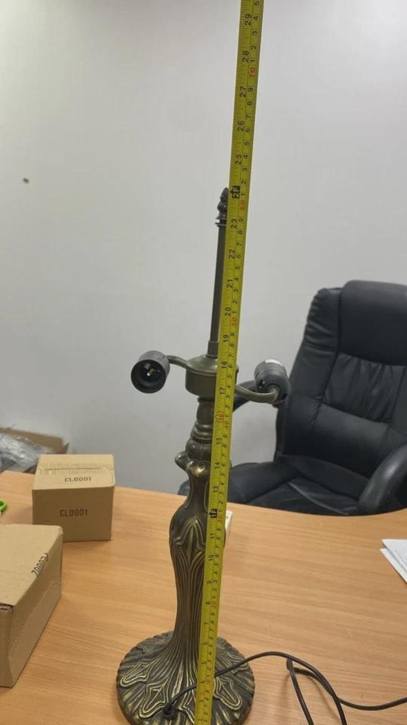 May include: An antique brass table lamp, approximately 29 inches tall, with a detailed floral base and two light sockets. The lamp is on a wooden desk, with a measuring tape alongside it.