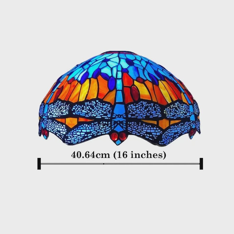 May include: A stained glass lamp shade with a dragonfly design. The shade is 16 inches wide and features a mosaic of blue, orange, and red glass pieces. The dragonfly's wings are outlined in black.