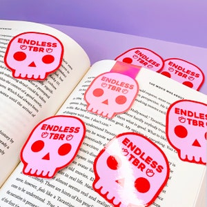 Könnte beinhalten: Sechs rosafarbene und rote Totenkopf-Lesezeichen mit dem Text "ENDLESS TBRO" auf jedem. Die Lesezeichen sind auf einem Buch angeordnet.