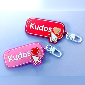 Peut inclure: Deux porte-cl&eacute;s avec le mot "Kudos" en blanc. L'un est rouge, l'autre rose, tous deux avec un c&oelig;ur et un curseur. Chaque porte-cl&eacute;s a un fermoir en m&eacute;tal blanc.
