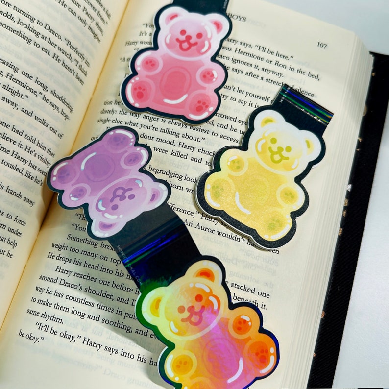Pu&ograve; includere: Quattro segnalibri a forma di orso gommoso in diversi colori: rosa, viola, giallo e arancione. Ogni segnalibro presenta un orso gommoso con un contorno nero e un viso sorridente.