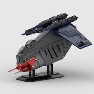 May include: A model spaceship made from toy bricks, predominantly grey and blue. It has a red and white front, two clear cockpit domes, and two dark blue missile launchers. The model is displayed on a black stand.