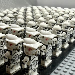 Puede incluir: Una gran colección de figuras de juguete blancas y negras, que se asemejan a soldados, dispuestas en filas. Cada figura tiene un casco blanco y marcas negras detalladas. Las figuras están sobre una base negra, con un fondo gris.