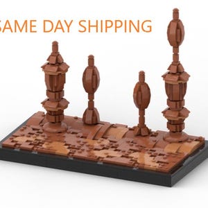 May include: A Lego model of a desert landscape with four brown towers. The towers are made of Lego bricks and have different shapes and sizes. The base of the model is a brown Lego baseplate.
