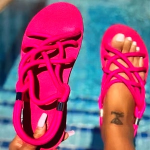 May include: A pair of bright pink sandals with a criss-cross strap design. The sandals are made of a soft, flexible material and have a comfortable fit.