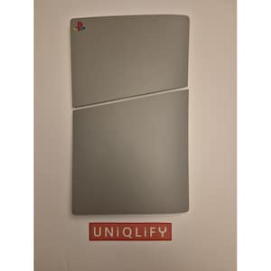May include: A gray PlayStation 5 console skin with the PlayStation logo in blue, red, and white. The skin is made of two pieces that fit together. The text "UNIQLIFy" is printed in red on a white background.