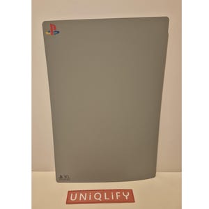 May include: A gray PlayStation 3 console skin with the PlayStation logo in the top left corner. The skin is made of a textured material and has a slight curve at the bottom.