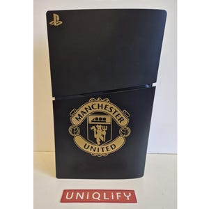 Könnte beinhalten: Schwarze PlayStation-Konsole mit goldenem Manchester United-Logo. Das PlayStation-Logo befindet sich oben links. Der Text "UNIQLIFY" steht unten.