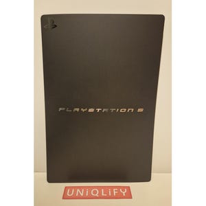 Puede incluir: Una caja de consola PlayStation 5 negra con el logotipo de PlayStation y el texto "PLAYSTATION 5" en plata.