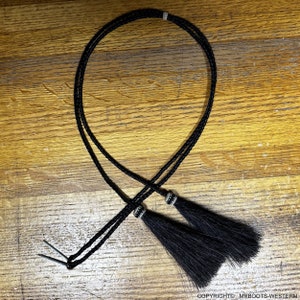 May include: Black braided leather bolo tie with silver accents and black horsehair tassels.