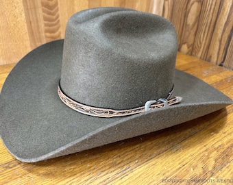 May include: A green felt cowboy hat with a brown leather band and a silver buckle. The hat has a wide brim and a tall crown.