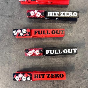 May include: A collection of five decorative clothespins. Each pin is red or black with white text that reads "FULL OUT" or "HIT ZERO." The pins are embellished with small casino-themed decorations.