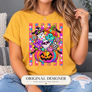 May include: A mustard yellow t-shirt featuring a vibrant graphic of a large, rainbow-colored jack-o'-lantern filled with colorful ghosts, candy, and bats. The design is set against a background of vertical pink stripes and multi-colored polka dots.