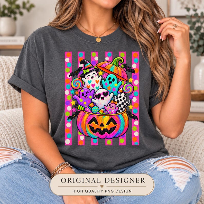 May include: A charcoal gray t-shirt featuring a vibrant graphic of a large, rainbow-colored jack-o'-lantern filled with colorful ghosts, lollipops, and candy. The design is set against a background of vertical pink and orange stripes with polka dots.