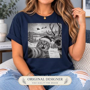 May include: A navy blue t-shirt featuring a black and white graphic print of a cat wearing a Santa hat taking a selfie with a reindeer in a snowy landscape, with a silhouette of Santa's sleigh and reindeer flying across the moonlit sky.