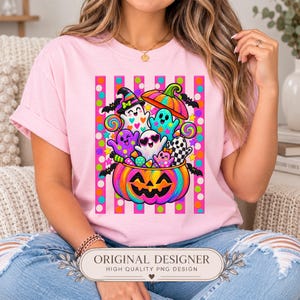 May include: A light pink t-shirt featuring a vibrant graphic of a large, colorful jack-o'-lantern filled with various cartoon ghosts, bats, and candy. The background of the print consists of bright pink vertical stripes and multi-colored polka dots.