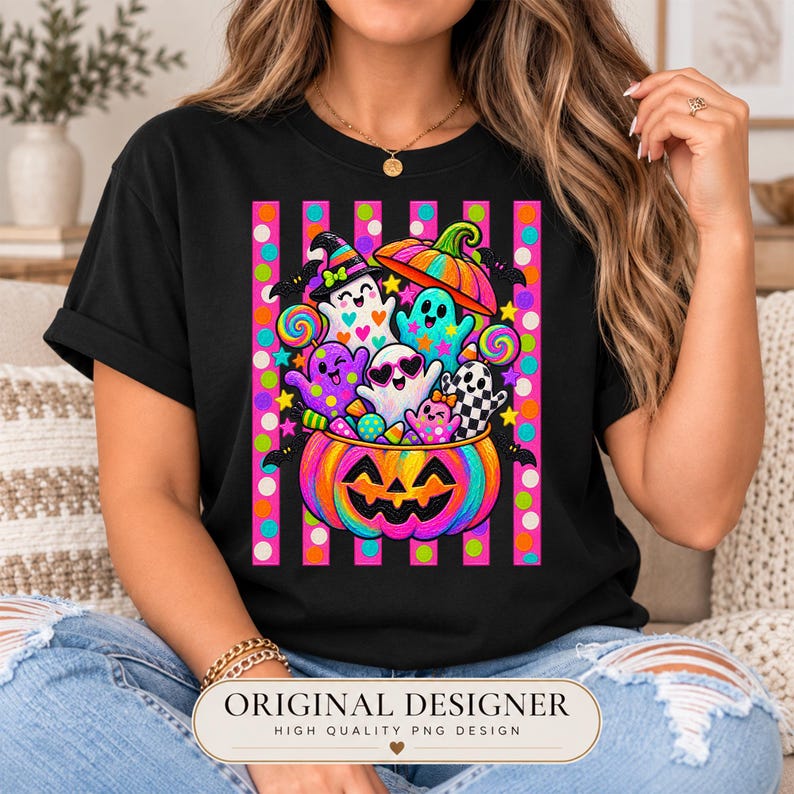 May include: A black t-shirt featuring a vibrant graphic of colorful ghosts and a jack-o'-lantern filled with candy. The design includes a background of pink and orange vertical stripes with polka dots, stars, and bats, creating a festive scene.