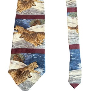 May include: A necktie featuring a repeating pattern of running wolves in a snowy landscape. The tie has alternating bands of burgundy, blue, and off-white with the wolf design. The tie is a standard width and length.