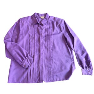 Puede incluir: Una camisa de manga larga de color morado con botones, un frente plisado y un cuello.