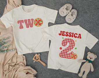 May include: Two off-white t-shirts with red gingham "TWO" and pizza graphics. One shirt has "JESSICA" and a gingham "2" with pizza. Accessories include bear slippers, a wooden rattle, and a stuffed bear.
