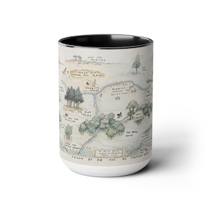 May include: A white ceramic mug with a black rim features a hand-drawn map of the Hundred Acre Wood from Winnie the Pooh. The map includes details like "Sandy Pit", "Rabbits House", "Six Pine Trees", and "100 Aker Wood". The text "Drawn by ME and MR SHEPARD" is at the bottom of the map.