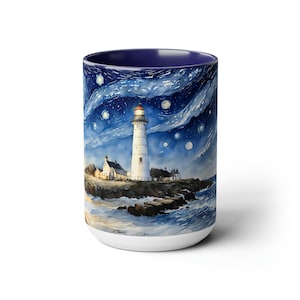 Op de afbeelding: Witte keramische mok met een aquarel schilderij van een vuurtoren onder een sterrenhemel. De vuurtoren staat op een rotsachtige kust met golven. De binnenkant van de mok is marineblauw.