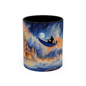 Op de afbeelding: Een witte keramische mok met een kleurrijke illustratie van een silhouet van Aladdin die op een magisch tapijt vliegt met een geest. De achtergrond is een sterrenhemel met een halve maan en een ver weg kasteel.